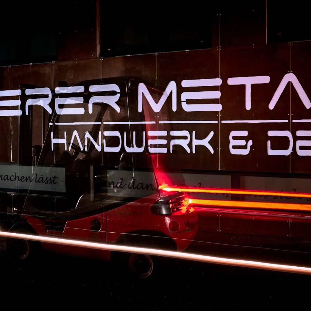 Langzeitbelichtung eines Staplers vor der Leuchtfassade eines Gewerbebetriebes.